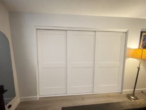 White shaker wood triple track sliding closet doors in a bedroom